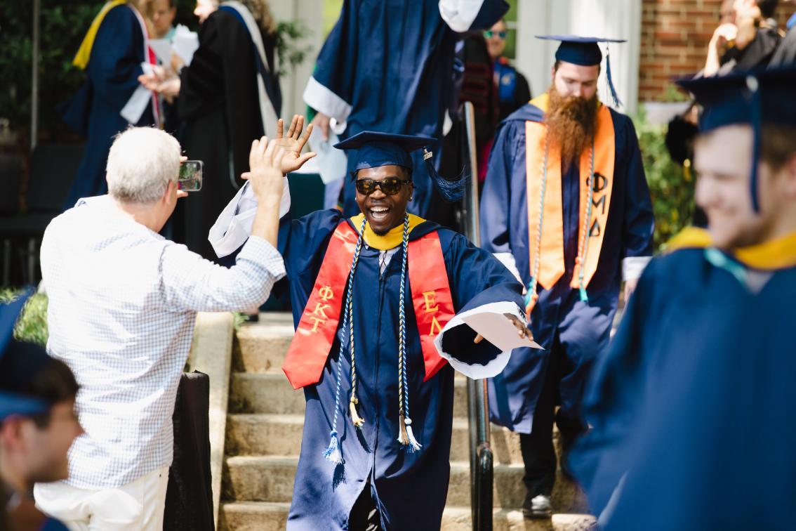 Student high fives a family member while passing after crossing the stage